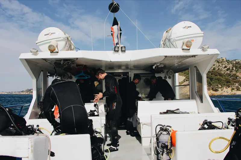 Divers and crew preparing equipment on a dive boat near a rocky coast