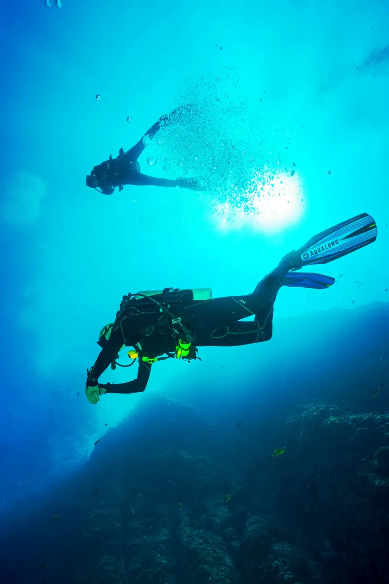 Two scuba divers descending in deep blue water